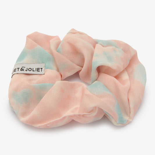 Bad hair day? Geen probleem want met deze vrolijke tie-dye scrunchie maak je van ieder kapsel een feestje!   De scrunchie is gemaakt van polyester en heeft een diameter van ongeveer 13cm. De stof heeft een roze met licht blauwe tie-dye effect.